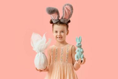 Paskalya hediyesi yumurtası ve pembe arka planda tavşanı olan tavşan kulaklı şirin bir kız.