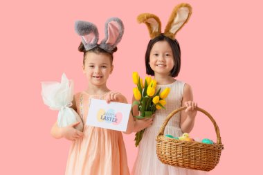 Paskalya yumurtaları ve pembe arka planda laleleri olan tavşan kulaklı şirin küçük kızlar.
