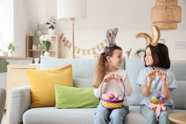 Paskalya yumurtaları evdeki kanepede oturan tavşan kulaklı şirin küçük kızlar.