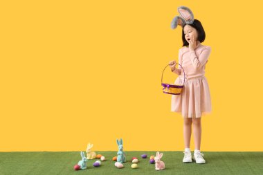 Tavşan kulaklı Asyalı kızı sepetle ve sarı arka planda Paskalya yumurtasıyla şoke ettim.