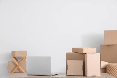 Beyaz duvarın yanındaki masada bir sürü farklı paket ve dizüstü bilgisayar var.