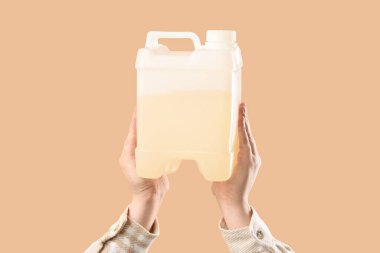 Kadın elleri bej arka planda teneke kutu tutuyor.