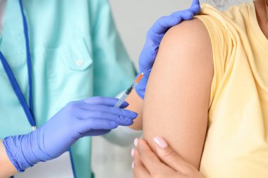 Kadın doktor klinikte genç bayana aşı yapıyor.