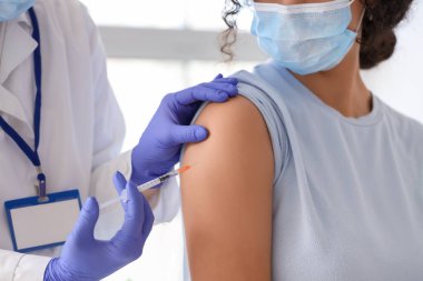 Kadın doktor klinikte genç bayana aşı yapıyor.