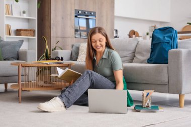 Not defteri ve dizüstü bilgisayarı olan genç kız evde çalışıyor.