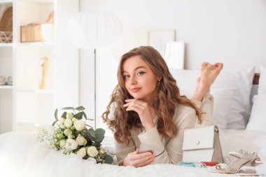 Düğün buketi ve aksesuarlarıyla güzel bir gelin yatak odasında yatıyor.