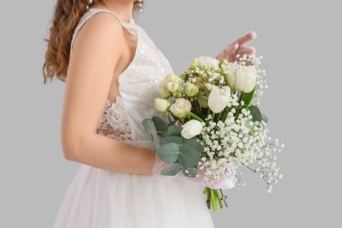 Gri arka planda çiçekleri olan beyaz gelinlikli güzel gelin, yakın plan.