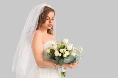 Gri arkaplanda çiçekler olan beyaz gelinlik içindeki güzel gelin.