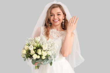 Gri arkaplanda çiçekler olan beyaz gelinlik içindeki güzel gelin.