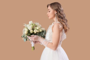 Bej arkaplanda çiçekler olan beyaz gelinlik içinde güzel bir gelin.