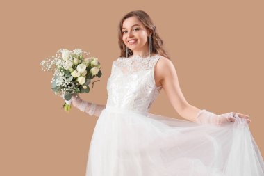 Bej arkaplanda çiçekler olan beyaz gelinlik içinde güzel bir gelin.