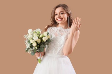 Bej arkaplanda çiçekler olan beyaz gelinlik içinde güzel bir gelin.