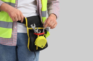 Gri arka planda profesyonel aletleri olan erkek inşaat işçisi, yakın plan