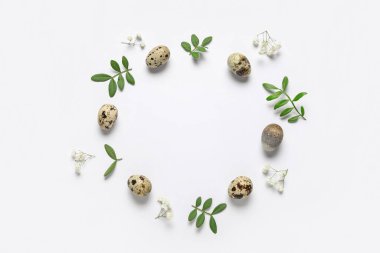 Paskalya yumurtalarından, çiçeklerden ve beyaz arka planda yeşil yapraklardan yapılmış çerçeve