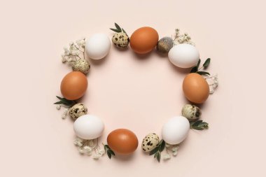 Paskalya yumurtaları, çiçekler ve bej arka planda yeşil yapraklardan yapılmış çerçeve, yakın plan