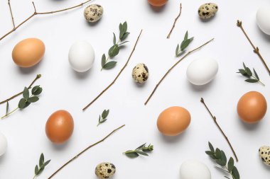 Beyaz arka planda Paskalya yumurtaları, dallar ve yeşil yapraklarla kompozisyon