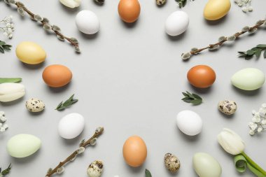 Frame made of Easter eggs, pussy willow branches, flowers and green leaves on grey background