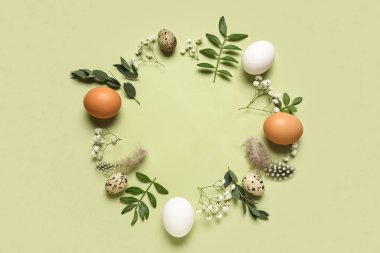 Paskalya yumurtaları, yeşil yapraklar, çiçekler ve yeşil arka plandaki tüylerden yapılmış çerçeve, yakın plan