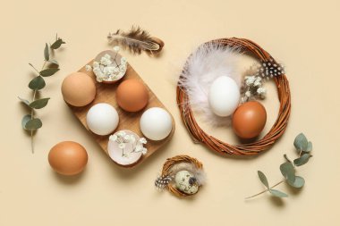 Çelenkli Paskalya yumurtaları, okaliptüs dalları ve bej arka planda tüyler.