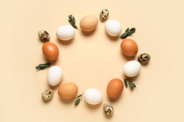 Paskalya yumurtası ve bej arkaplanda yapraklardan yapılmış çerçeve