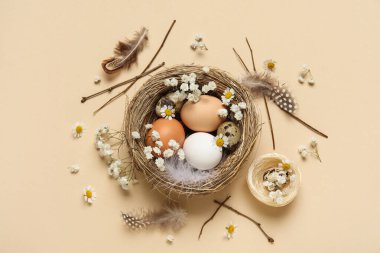 Paskalya yumurtaları, çiçekler ve bej arka planda tüyleri olan bir yuva.