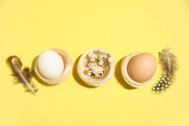 Sarı arka planda Paskalya yumurtaları, çiçekleri ve tüyleri olan yuvalar