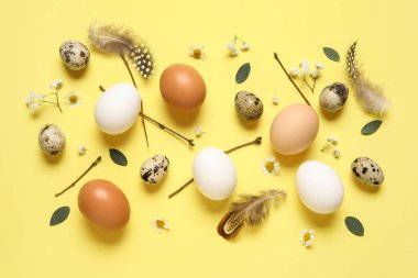 Sarı arka planda Paskalya yumurtaları, çiçekler, tüyler ve dallarla kompozisyon