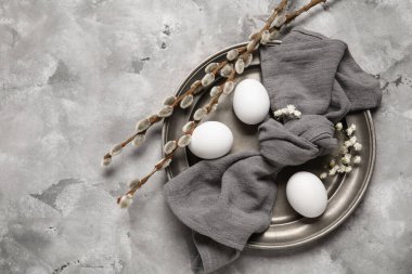 Paskalya yumurtaları, söğüt dalları, çiçekler ve gri grunge arka planda peçeteyle şenlik masası.