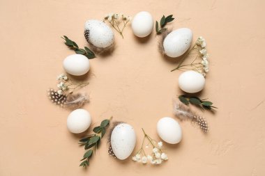 Paskalya yumurtaları, tüyler, yapraklar ve bej renginde çiçeklerden yapılmış çerçeve
