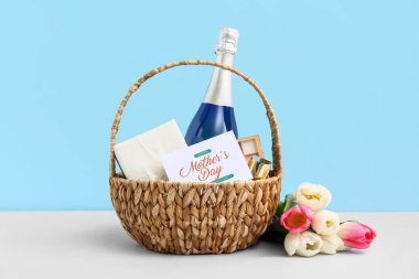 Anneler Günü için lale, şampanya şişesi ve kozmetik sepetleri mavi arka planda beyaz masada.