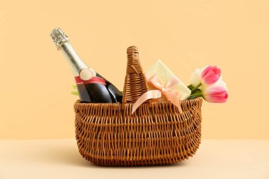 Laleli sepet, şampanya şişesi ve bej arka planda hediye kutusu.