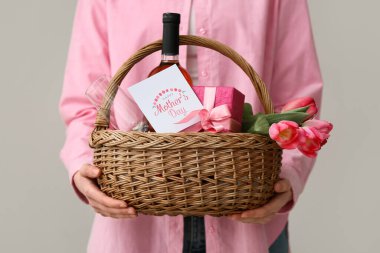 Beyaz arka planda Anneler Günü için elinde şarap şişesi, lale ve hediye kutusu olan genç bir kadın var.