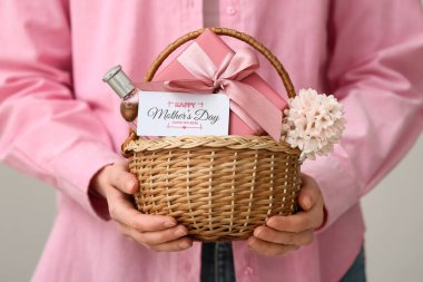 Beyaz arka planda Anneler Günü için çiçek, hediye kutusu ve parfüm taşıyan genç bir kadın.