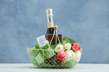 Anneler Günü için şampanya şişesi, lale ve çikolata dolu sepet mavi grunge arka planda.