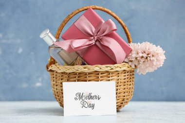 Çiçekli sepet, Anneler Günü için hediye kutusu ve parfüm mavi grunge arka planına karşı masada.