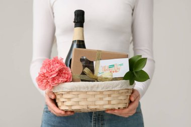 Beyaz arka planda Anneler Günü için karanfilli, şampanya şişeli ve çikolatalı sepet taşıyan genç bir kadın.