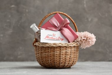 Üzerinde çiçek, hediye kutusu ve Anneler Günü için parfüm olan sepet gri grunge arka planda.