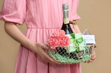 Elinde şampanya şişesi, karanfil ve bej arka planda Anneler Günü için hediye paketi olan genç bir kadın.