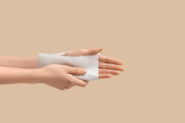 Bej arka planda kağıt peçeteyle ellerini silen genç bir kadın, yakın plan.