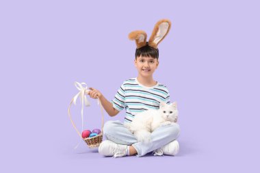 Paskalya sepeti ve leylak arka planda oturan beyaz kediyle tavşan kulaklı şirin bir çocuk.