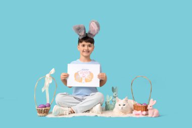 Tebrik kartı, Paskalya sepeti ve mavi arka planda beyaz kedisi olan tavşan kulaklı şirin bir çocuk.