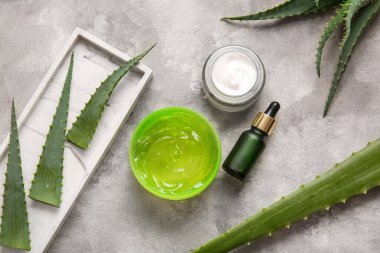 Gri arkaplanda aloe vera yaprakları olan farklı kozmetik ürünler