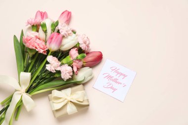 Bir buket farklı güzel çiçek, tebrik kartı ve bej arka planda hediye kutusu. Anneler Günü kutlaması