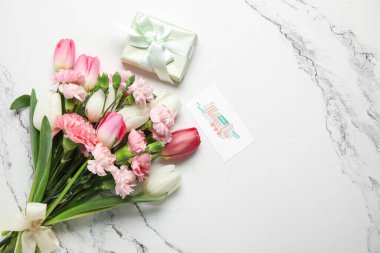 Tebrik kartı ve beyaz arka planda hediye kutusu olan farklı güzel çiçeklerden oluşan bir buket. Anneler Günü kutlaması