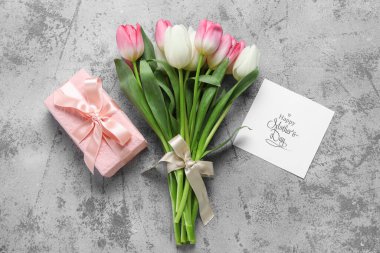 İçinde tebrik kartı ve gri arka planda hediye kutusu olan bir buket güzel lale çiçeği. Anneler Günü kutlaması