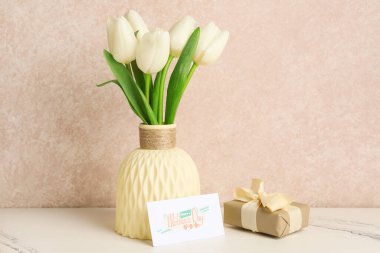 İçinde bir buket güzel lale çiçeği, tebrik kartı ve hediye paketi olan bir vazo. Anneler Günü kutlaması