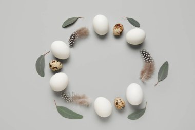 Yapraklı tüy, tavuk ve bıldırcın yumurtalarından yapılmış çerçeveler gri arka planda. Paskalya kutlaması
