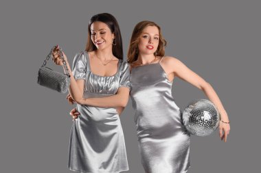 Gri arka planda disko topu olan gümüş elbiseli şık genç kadınlar.