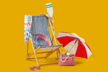 Güverte sandalyesi, şişme yüzük, yaz çantası ve sarı arka planda plaj şemsiyesi. Tatil kavramı