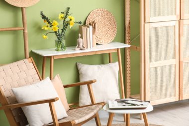 Oturma odasındaki yeşil duvarın yanında dergileri ve kitapları olan güzel nergis çiçekleri vazosu.